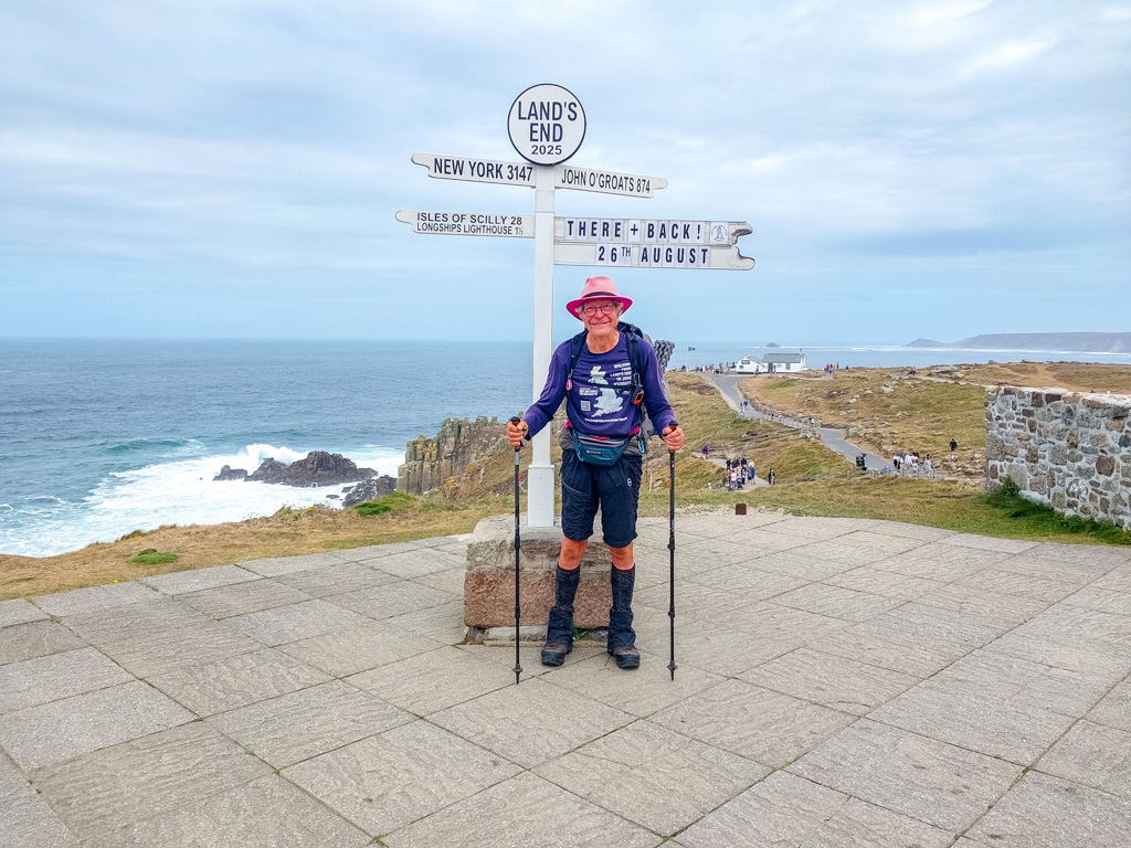 <center>2508-0048 - Chris standing under Land's End signpost (taken by Sam Murphy) -  August 26, 2025  <br>  (1/550 sec at f / 1.8 ISO 20    4 mm) </center>